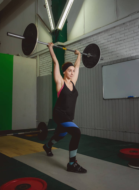 Strong woman lifting barbell as a part of crossfit exercise routine - Photo, Image