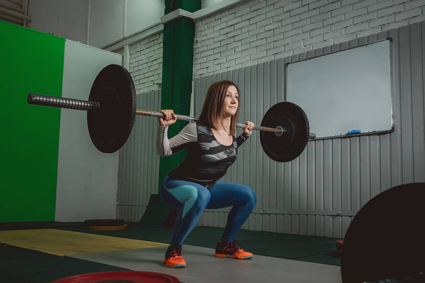 Strong woman lifting barbell as a part of crossfit exercise routine - Фото, изображение