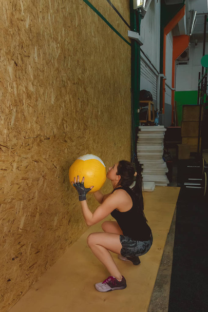 Young fit woman exercising by throwing a ball up in a gym - Фото, зображення