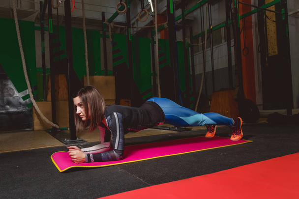 Attractive young woman is doing plank exercise while working out in gym - Foto, afbeelding