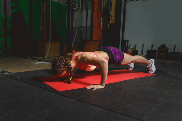 Attractive young woman is doing plank exercise while working out in gym - Foto, immagini
