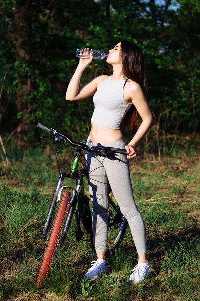 Молодая смешанная гонка женщина-велосипедистка на горном велосипеде питьевой воды во время велоспорта тренировки на открытом воздухе
. - Фото, изображение