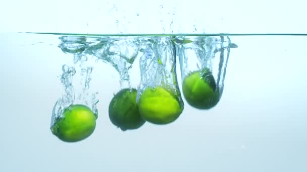Limes wrzucenie do wody na niebieskim tle w zwolnionym tempie. - Materiał filmowy, wideo