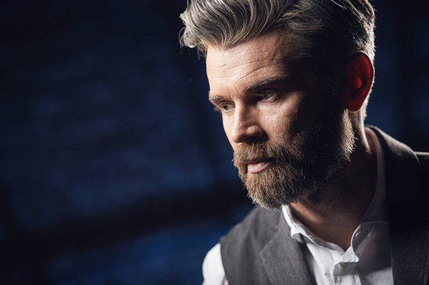 Closeup portrait of handsome serious charismatic man with beard, in white shirt and black classic waistcoat in studio on dark  background - Foto, Imagem