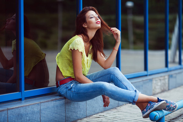 Smiling hipster girl in blue jeans in the summer city. - Fotó, kép