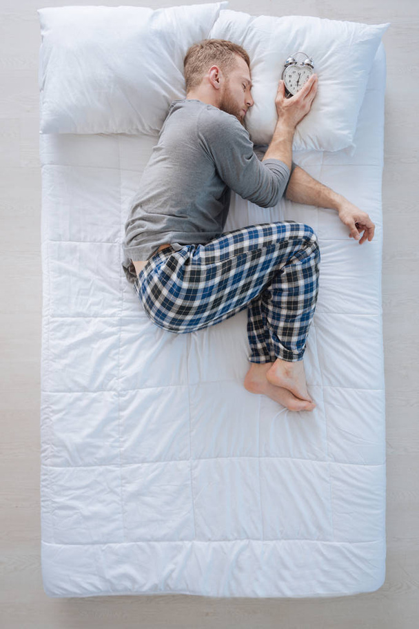 Мирный приятный человек кладет будильник на подушку
 - Фото, изображение