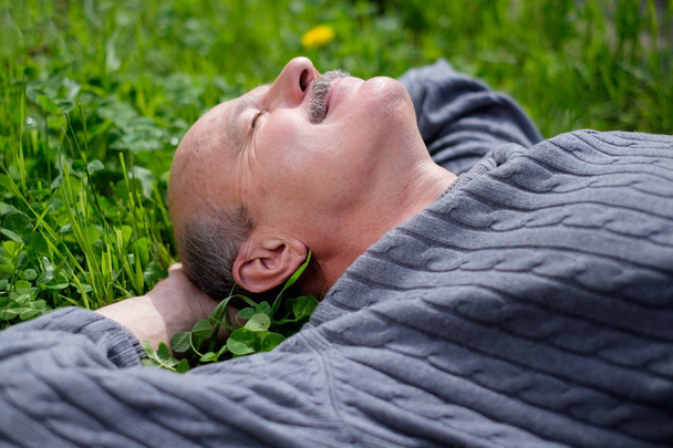 Homem feliz maduro deitado na grama verde. Ele segura a folha de cebola na boca e fecha os olhos
. - Foto, Imagem
