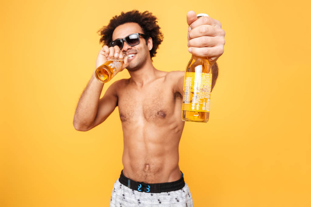 Portrait of a african man in sunglasses showing beer bottle - Foto, imagen