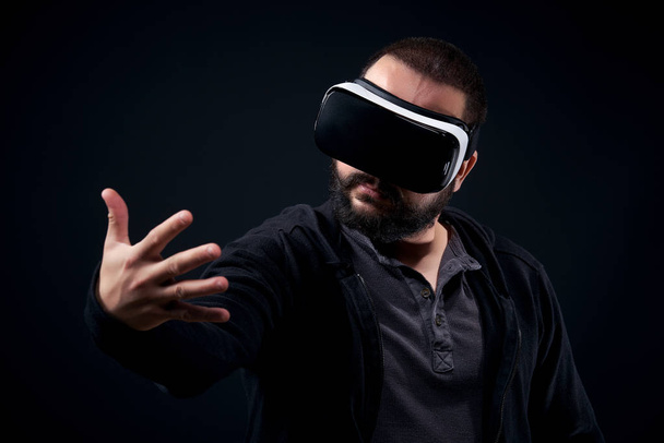 Young hipster bearded man wearing virtual reality goggles. Black background studio VR concept - Foto, Imagen