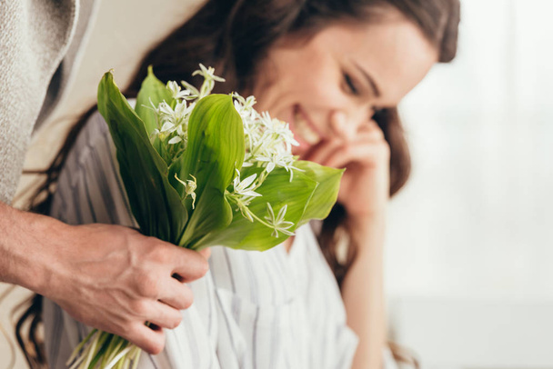 man presenting flowers to girlfriend at home - 写真・画像