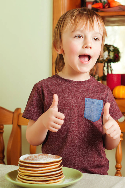 Lindo niño comiendo una pila de panqueques en la cocina
. - Foto, Imagen