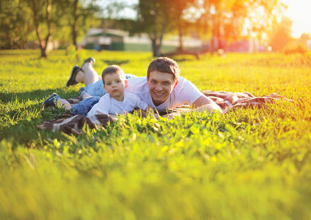 Sunny portrait happy father with son child lying on the green gr - Φωτογραφία, εικόνα