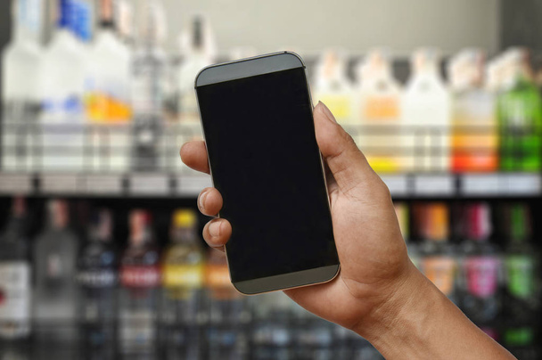 ένα χέρι που κρατά το smartphone στο σούπερ μάρκετ κρασί κατάστημα - Φωτογραφία, εικόνα