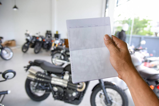 a hand holding saving account bank book on motorcycle showroom - Foto, immagini