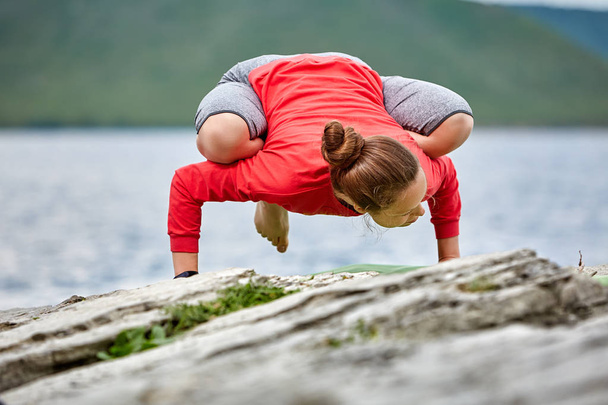 Young woman doing yoga pose arm balance on the stone near big river. - Photo, Image