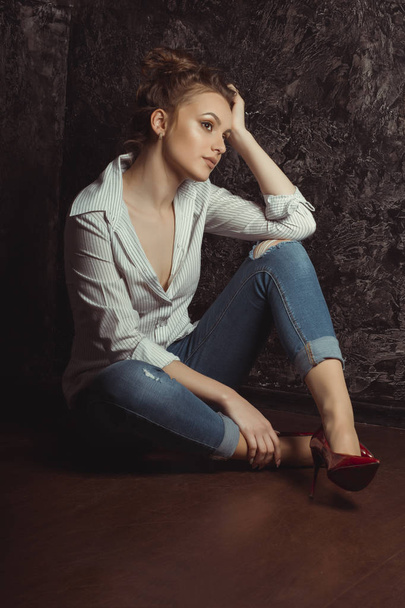 Lovely young woman in shirt and jeans sitting on the floor - Foto, afbeelding