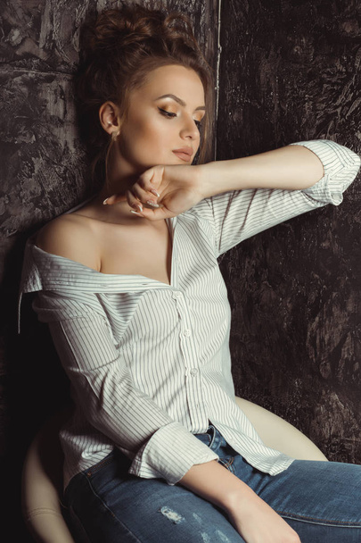 Lovely young model sitting on a chair  in striped and torn jeans - Valokuva, kuva