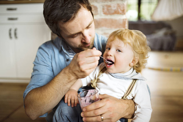 Young father at home feeding his little son with yoghurt. - Foto, imagen