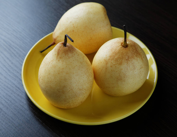 Three yellow pears on the plate on the table - 写真・画像