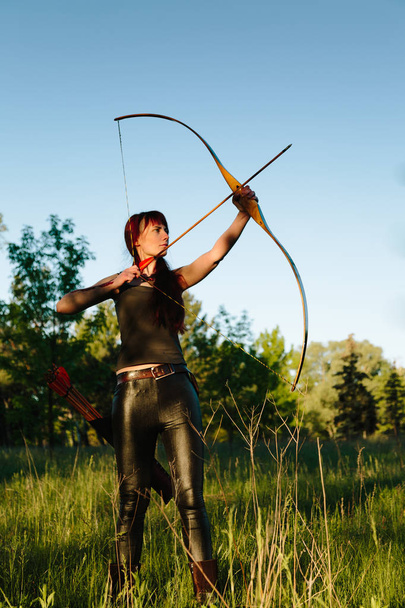 Female ginger hair archer shooting targets with her bow and arrow. Concentration, target, success concept. - Photo, Image