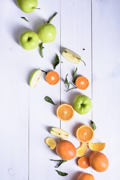 Fresh ripe fruits on a white table. Oranges and green apples sli - Photo, Image