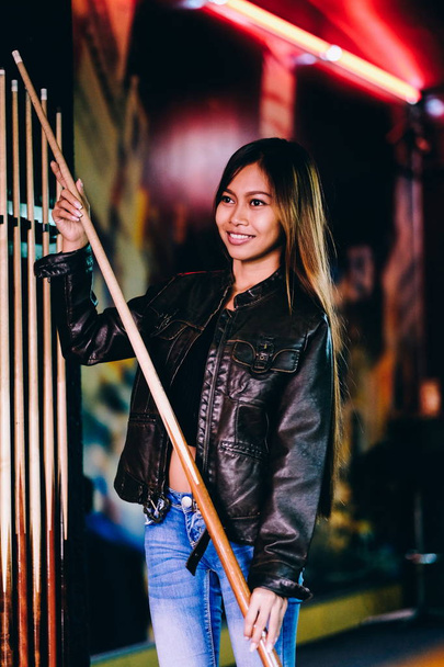 junges schönes Mädchen in Lederjacke in einem Billardclub, mit Cue-Stick, das sich auf das Spiel vorbereitet - Foto, Bild
