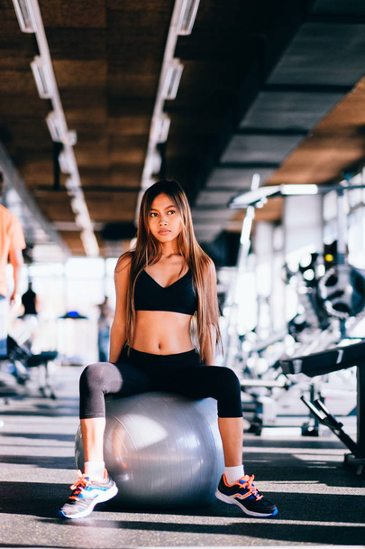 Mujer joven fitness con el pelo largo en el gimnasio, sentado en la pelota de Pilates
 - Foto, Imagen