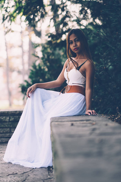 Beautiful girl in long white dress sitting, daydreaming in the park  - Φωτογραφία, εικόνα
