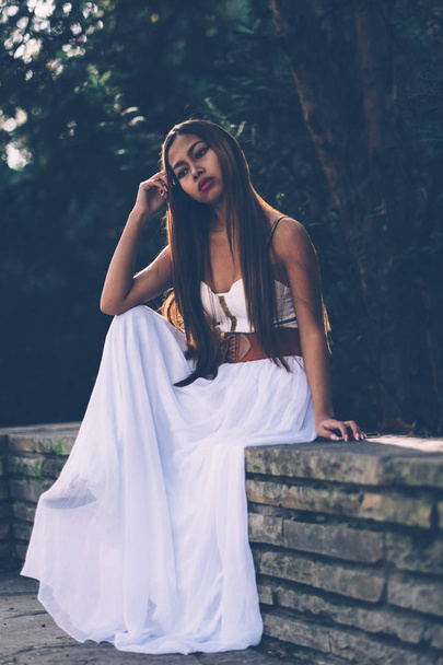 Beautiful girl in long white dress sitting, daydreaming in the park  - Foto, afbeelding
