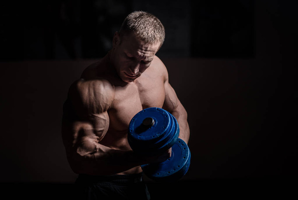 Muscular bodybuilder guy doing exercises with dumbbell over black background - Foto, afbeelding