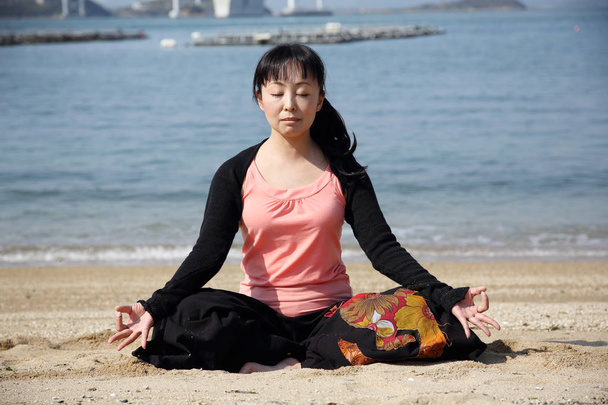 Japanse vrouw yoga zittend op een strand - Foto, afbeelding