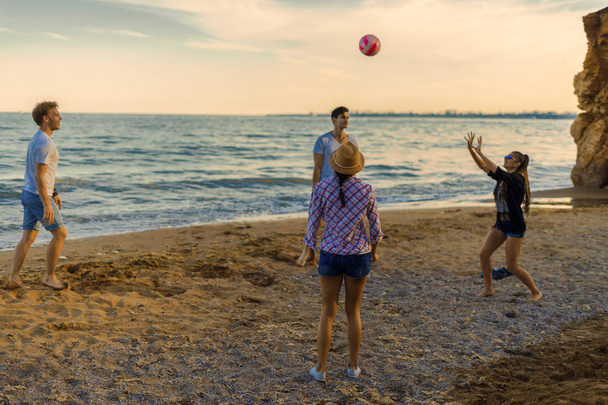 friends playing volleyball on a wild beach during sunset - Fotó, kép