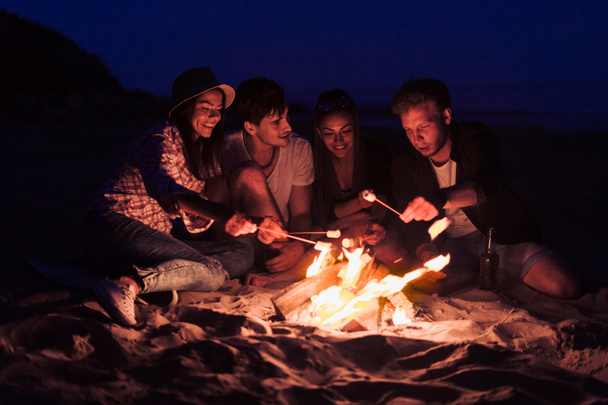 friends sitting on the beach clink glasses near bonfire - Fotografie, Obrázek