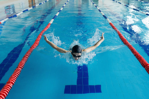 Young girl in goggles and cap swimming butterfly stroke style in the blue water pool. - Photo, Image
