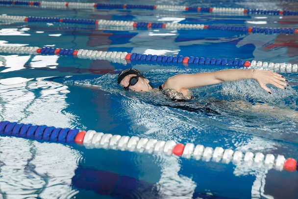 Молода дівчина в окулярах і кепці для плавання стиль повзання в басейні з блакитною водою
. - Фото, зображення