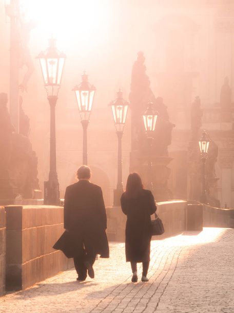 Man and woman couple walk on Charles Bridge in foggy morning, Prague, Czech Republic. Romantic Prague theme - Zdjęcie, obraz