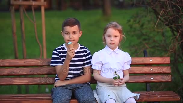 男の子と女の子がベンチに座っています。公園と打撃のタンポポの周りを実行します。 - 映像、動画