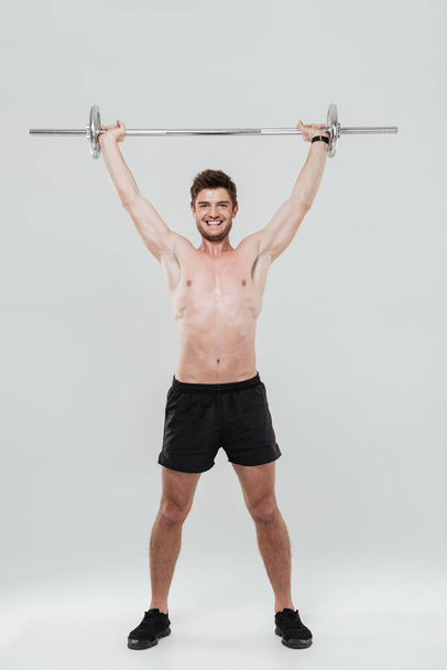 Full length portrait of a fit sportsman lifting heavy barbell - Foto, afbeelding