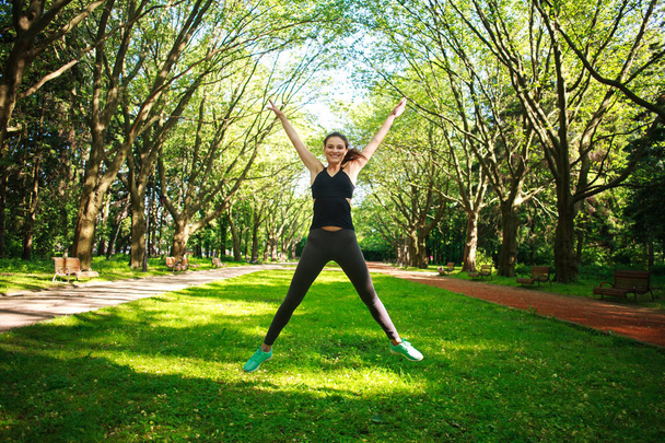 Sportive young fitness woman jumping in summer park - Fotoğraf, Görsel