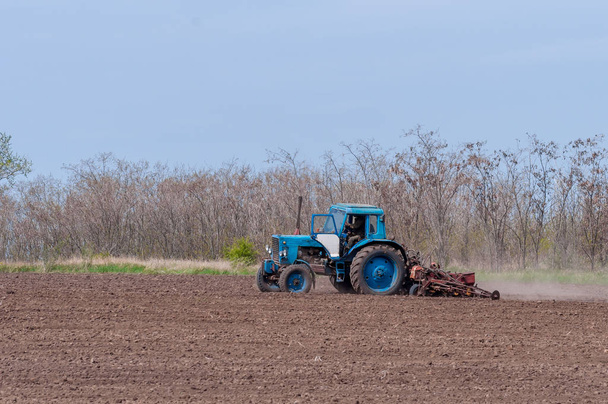 Старый трактор в поле пашет землю. Весенний пейзаж сельской местности, ферма
. - Фото, изображение