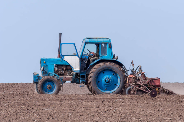 Старый трактор в поле пашет землю. Весенний пейзаж сельской местности, ферма
. - Фото, изображение