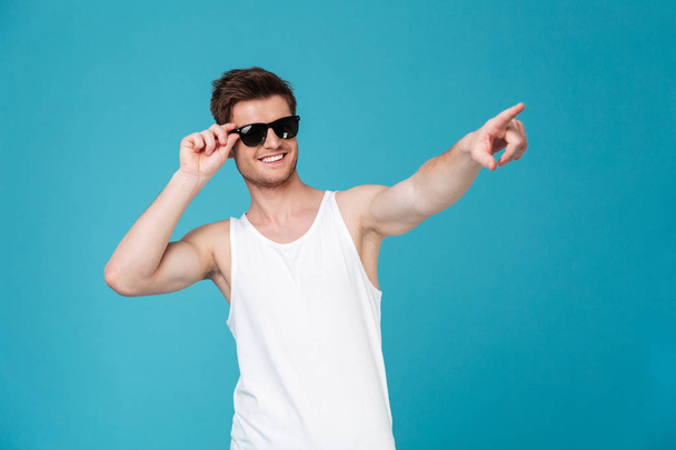 Cheerful guy in sunglasses and singlet pointing finger - Fotoğraf, Görsel