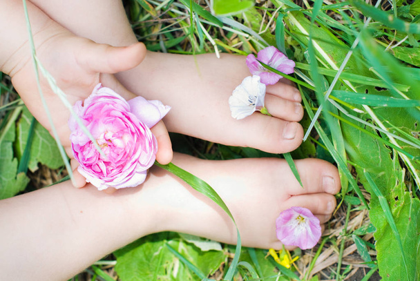 Yaz yeşil çimlere oturup ayaklarını çiçekler çocuk. - Fotoğraf, Görsel