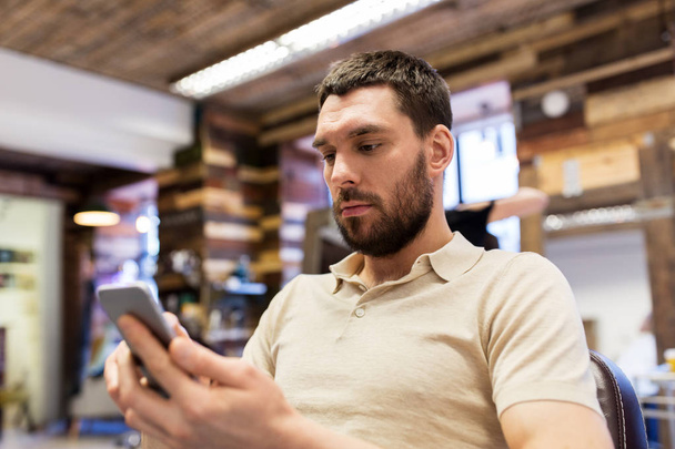man with smartphone at barbershop or salon - Photo, Image