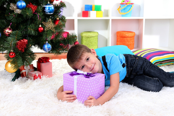 Little boy lying on gift in his hands under Christmas Tree waiting for Santa Claus to come - Fotoğraf, Görsel
