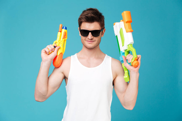 Positive man looking camera and holding two water guns - Fotoğraf, Görsel