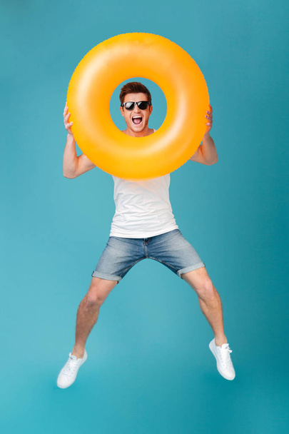 Happy excited man in sunglasses holding inflatable ring and jumping - Fotografie, Obrázek
