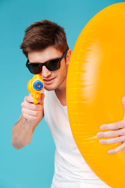 Man holding inflatable ring and pointing water gun at camera - Foto, afbeelding