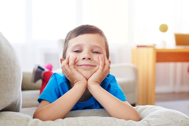 Young smiling boy lying on sofa and leaning on his hands - Photo, Image