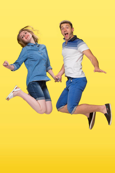 Portrait of a young couple jumping against yellow background - Foto, immagini